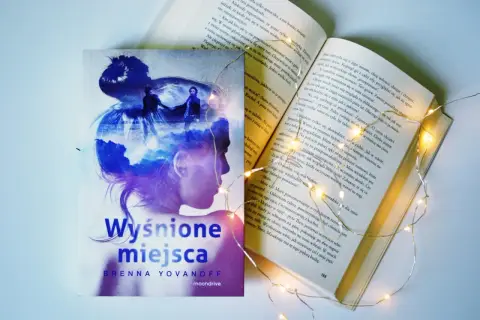 Osoba na okładce książki "Wyśnione miejsca" Brenny Yovanoff, otoczona magicznymi światełkami.