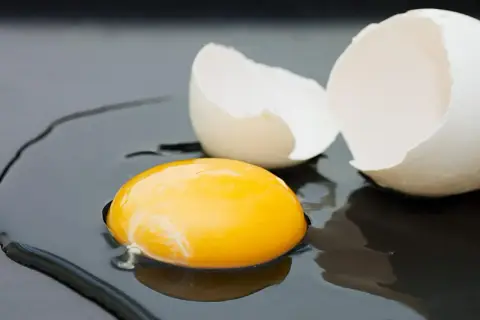 Rozbite jajko na ciemnym tle. Żółtko lśni, a skorupka czeka na usmażenie. Zastanawiasz się nad jajko smażone kcal?