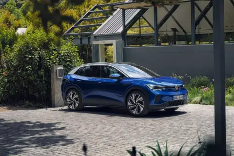 Niebieski VW ID.4 ładuje się przy nowoczesnym domu. Elektryczny SUV stoi na podjeździe, podłączony do ładowarki.
