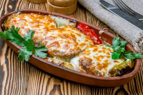 Kotlet po góralsku zapieczony z serem i warzywami w glinianym naczyniu, udekorowany natką pietruszki.