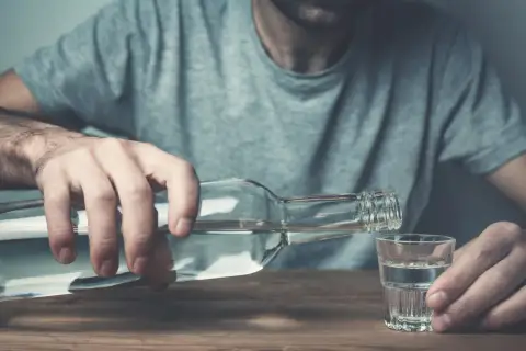 Mężczyzna nalewa alkohol do kieliszka. To może być jeden z objawów przed śmiercią alkoholika, symbol jego walki.