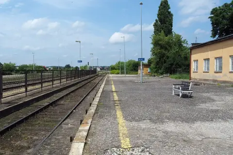 Pusta stacja kolejowa Opoczno Kielce. Torowisko, peron z ławką i żółtą linią, budynek dworca.