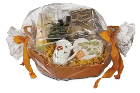 Ein liebevoll zusammengestelltes Geschenk, das mit Folie und orangefarbenen Bändern verpackt ist. Darin befinden sich Tassen, Pasta und weitere Leckereien.