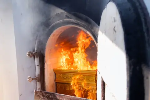 Złota trumna płonie w piecu kremacyjnym, a płomienie tańczą wokół. Czy kości się palą? To pytanie towarzyszy tej scenie.