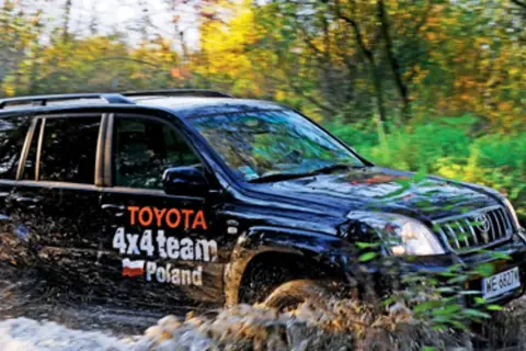 Czarny Toyota Land Cruiser 100 z napisem "4x4 team Poland" pokonuje błotnistą trasę w lesie.