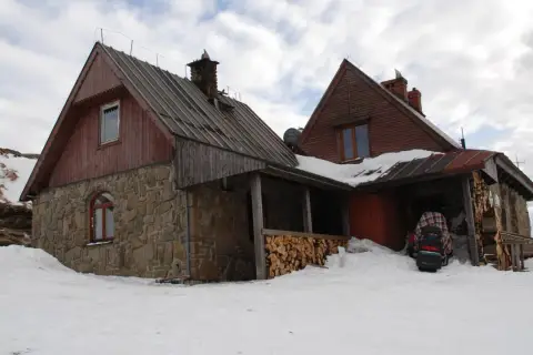 Kamienna Chatka Puchatka w Bieszczadach, zasypana śniegiem, z drewnianym zadaszeniem i stosem drewna.