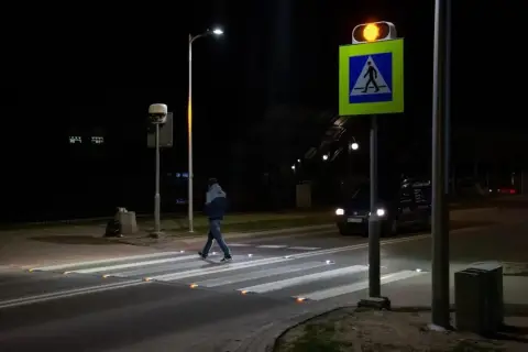 Nocą pieszy przechodzi przez pasy, oświetlone odblaskami. Obok miga żółte światło sygnalizatora, a znak d6 przypomina o obowiązku ustąpienia pierwszeństwa.