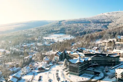 Malowniczy hotel ze stokiem w zimowej scenerii. Śnieg pokrywa dachy domów i drzewa, tworząc bajkowy krajobraz.