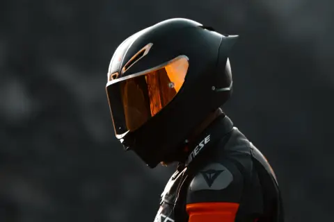 Un motociclista indossa un casco integrale nero con visiera arancione riflettente, pronto per la pista.