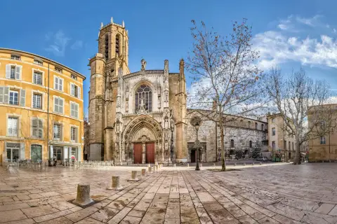 Katedra w Aix-en-Provence, z żółtą kamienicą obok, na brukowanym placu pod błękitnym niebem.