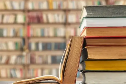 Stos książek na tle biblioteki. Unikaj chaosu w nazewnictwie zakładek w dużym projekcie literackim, by nie zgubić wątku.