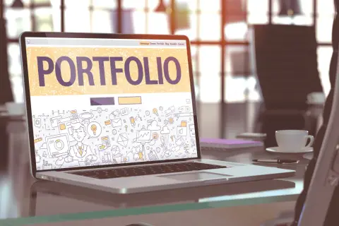 Laptop z napisem "PORTFOLIO" i rysunkami symbolizującymi pracę kreatywną. To świetny przykład, portfolio co to jest.
