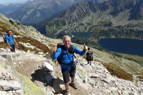 Uśmiechnięty turysta na kozi wierch trasie, z kciukiem w górze. W tle piękne Tatry i dwa jeziora.