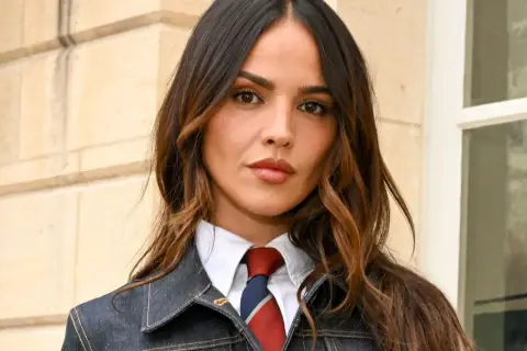 Mujer con cabello castaño y mechas woodlights, viste camisa blanca, corbata y chaqueta vaquera.