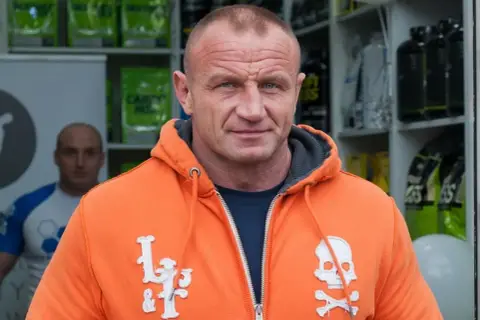 Mariusz Pudzianowski, znany jako Pudzian, w pomarańczowej bluzie z kapturem. Ile lat ma Pudzian? To pytanie nurtuje wielu fanów.