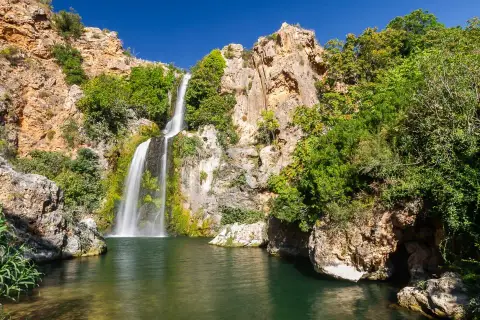 El Salto de Chella, una cascada imponente rodeada de rocas y vegetación exuberante, cae en una poza de agua verde.