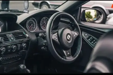 Wnętrze BMW E64 z czarną kierownicą, deską rozdzielczą i karbonowymi wstawkami.