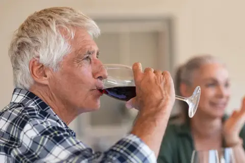 Un homme âgé boit du vin rouge. Attention, le vin périmé présente un danger.