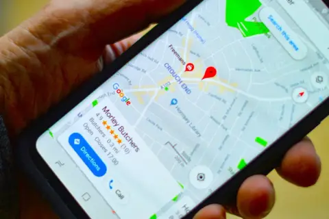 Dłoń trzyma smartfon z mapą Google. Widoczna jest pinezka Google wskazująca lokalizację "Morley Butchers".