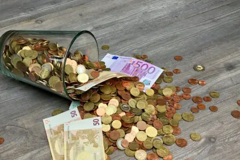 Słoik z monetami i banknotami, w tym 500 euro, rozsypany na drewnianej podłodze. To waluta Francji i innych krajów strefy euro.