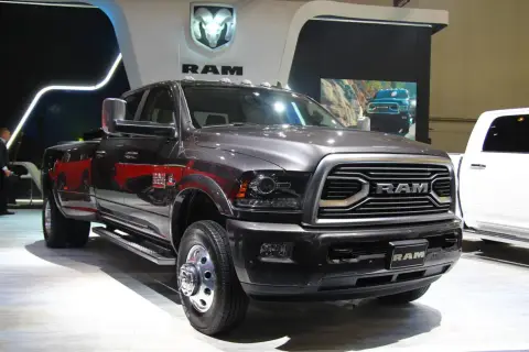 Ciemnoszary Dodge Ram 3500 z podwójnymi tylnymi kołami prezentuje się na wystawie, obok białego pickupa.