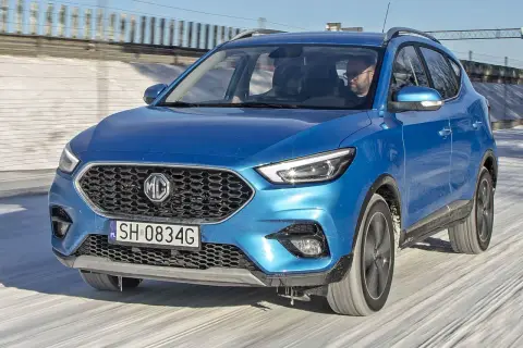 Niebieski MG ZS Classic jedzie po zaśnieżonej drodze. Kierowca w okularach prowadzi auto.