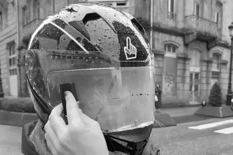 Mano colocando el Pinlock en un casco de moto mojado por la lluvia, listo para instalar.