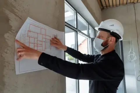 Mężczyzna w kasku i masce analizuje projekt budowlany. Dbałość o szczegóły, jak podczas studiów BHP, zapewnia bezpieczeństwo.