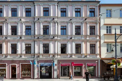 Kamienica przy ul. Piotrkowskiej 61 w Łodzi. Elegancka fasada z licznymi oknami i zdobieniami. Na parterze sklepy, m.in. jubiler i bank.