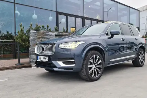 Elegancki, ciemnoszary Volvo XC90 T8 z nowoczesnymi światłami LED stoi przed budynkiem z dużymi, przeszklonymi oknami.