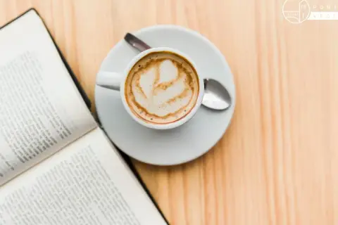 Un libro aperto e una tazza di caffè con schiuma, un invito al caffè illuminismo, su un tavolo di legno.