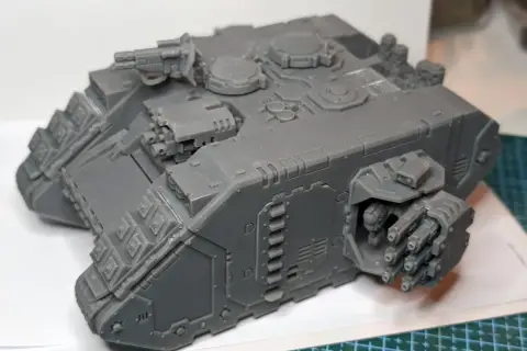 Szary model Land Raider Redeemer, gotowy do malowania, z działkiem na dachu i wyrzutniami flamerów po bokach.