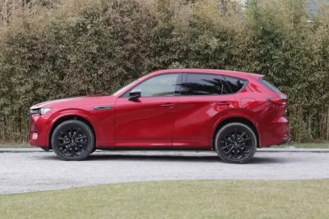 Czerwona Mazda CX-60 3.3 diesel z czarnymi felgami stoi na żwirowej drodze, za nią gęsty żywopłot.