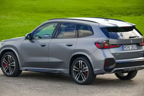 Grauer BMW X1 23d steht auf Asphalt vor grüner Wiese.