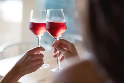 Dwie osoby wznoszą toast kieliszkami z różowym winem. Czy wino różowe powstaje z mieszania białego z czerwonym? Proces produkcji jest ciekawy!