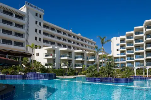 Basen hotelowy Capo Bay w Protaras z palmami i białymi budynkami hotelowymi pod błękitnym niebem.