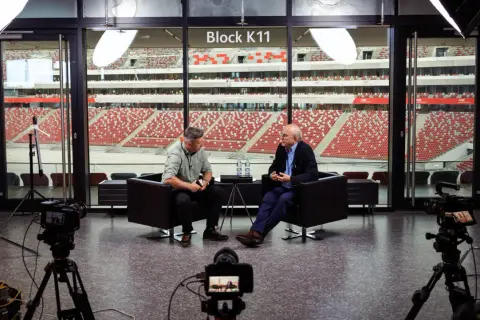 Tomasz Tomaszewski rozmawia z mężczyzną na tle stadionu.