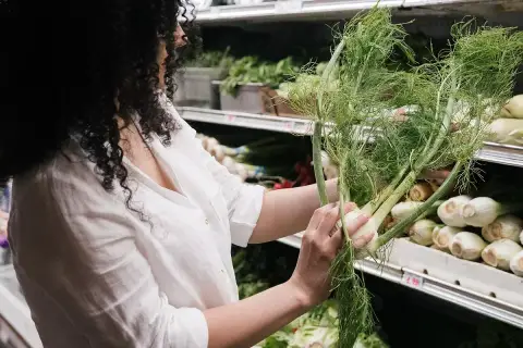 Mujer con cabello rizado elige hinojo fresco, reconociendo sus maravillosas propiedades para la salud.