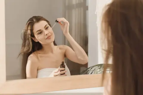 Kobieta aplikuje serum na twarz, zastanawiając się, czy niacynamid można łączyć z kwasem azelainowym.