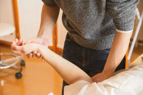 Fizjoterapeuta delikatnie masuje krzywą rękę po zdjęciu gipsu, pomagając przywrócić jej pełną sprawność.