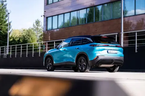 Błękitny BAIC 5 z czarnym dachem stoi przed nowoczesnym budynkiem.