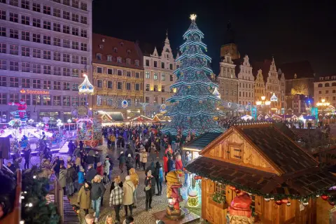 Tłoczny jarmark we Wrocławiu nocą. Rozświetlona choinka, kramy i tłumy ludzi tworzą magiczną atmosferę.