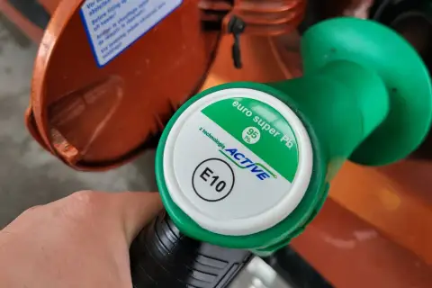 Dłoń trzyma zielony pistolet dystrybutora paliwa z oznaczeniami 95 Pb i E10.