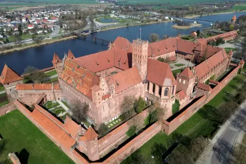 Malbork, największy zamek na świecie, z czerwonej cegły, otoczony murami obronnymi, nad rzeką Nogat.