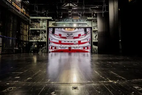 Widok na pustą widownię z czerwonymi fotelami i balkonami, widziany ze sceny. To wnętrze teatru dramatycznego w Warszawie, gotowe na spektakl.