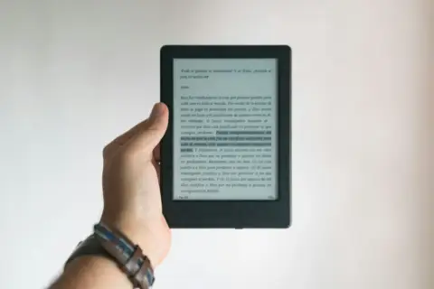 Dłoń trzyma czytnik e-booków. Tekst na ekranie dotyczy zasad ochrony praw autorskich przy wydawaniu e-booków.