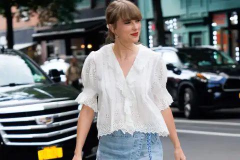 Chica con estilo "clean girl" con blusa blanca bordada y falda vaquera, paseando por la ciudad.