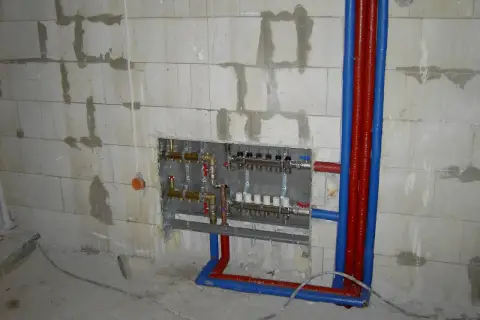 Instalacja hydrauliczna przed tynkami: widoczny rozdzielacz ogrzewania podłogowego i rury w ścianie z bloczków.