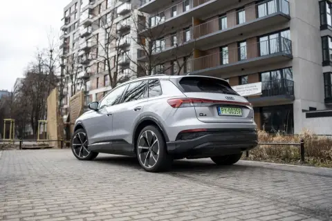 Srebrny Audi Q4 elektryk z zieloną tablicą rejestracyjną stoi na brukowanym podjeździe przed nowoczesnym budynkiem mieszkalnym.