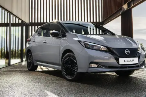 Szary Nissan Leaf stoi przed nowoczesnym budynkiem z przeszklonymi ścianami.
